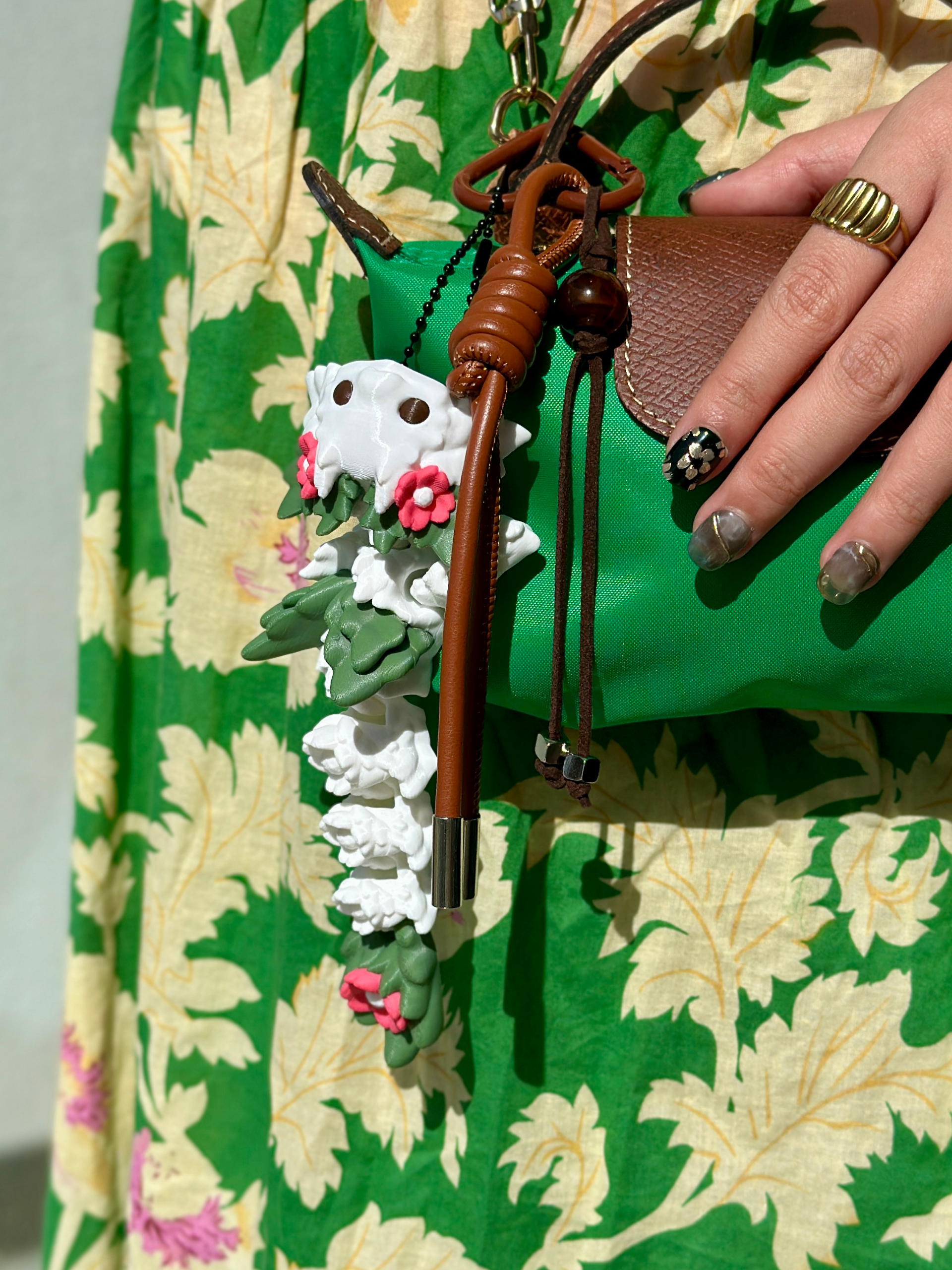 White 3D printed flower dragon bag charm with pink flowers and green leaf-like spots, hanging on a green bag