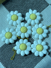 Several daisy flower clicker keychains arranged on a surface, showing their white petal design and yellow centers