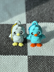 3D printed blue goose and white goose bag charms placed next to each other with orange and yellow beaks and feet