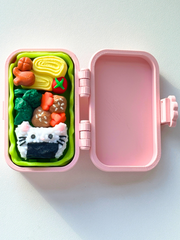 Open pink 3D printed bento box fidget toy displaying three detailed food-themed clickers inside: cat onigiri, karaage with vegetables, and tamagoyaki with sides