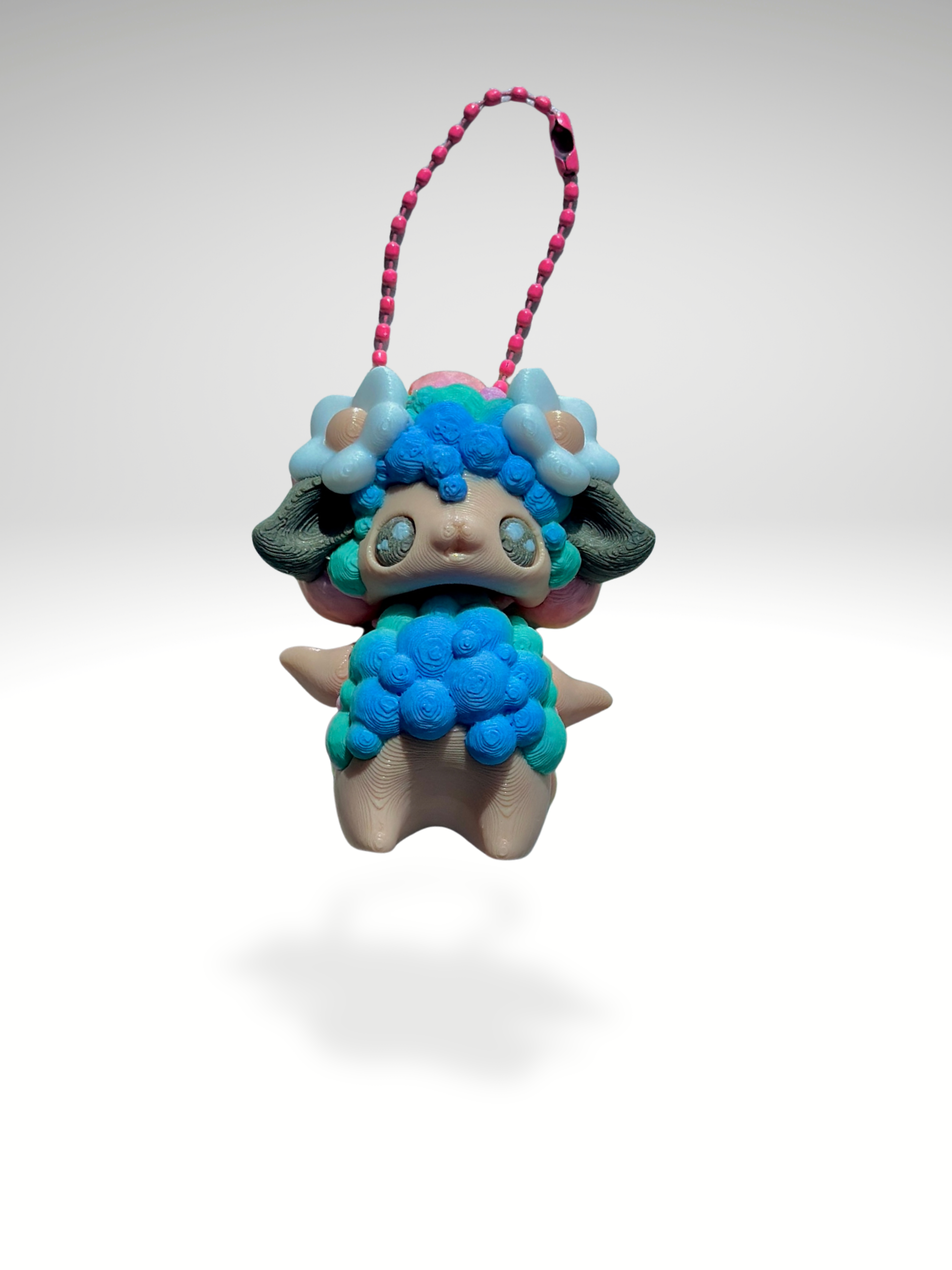 Close-up of 3D printed pastel rainbow sheep bag charm with white background, showing flower accents and rounded shape
