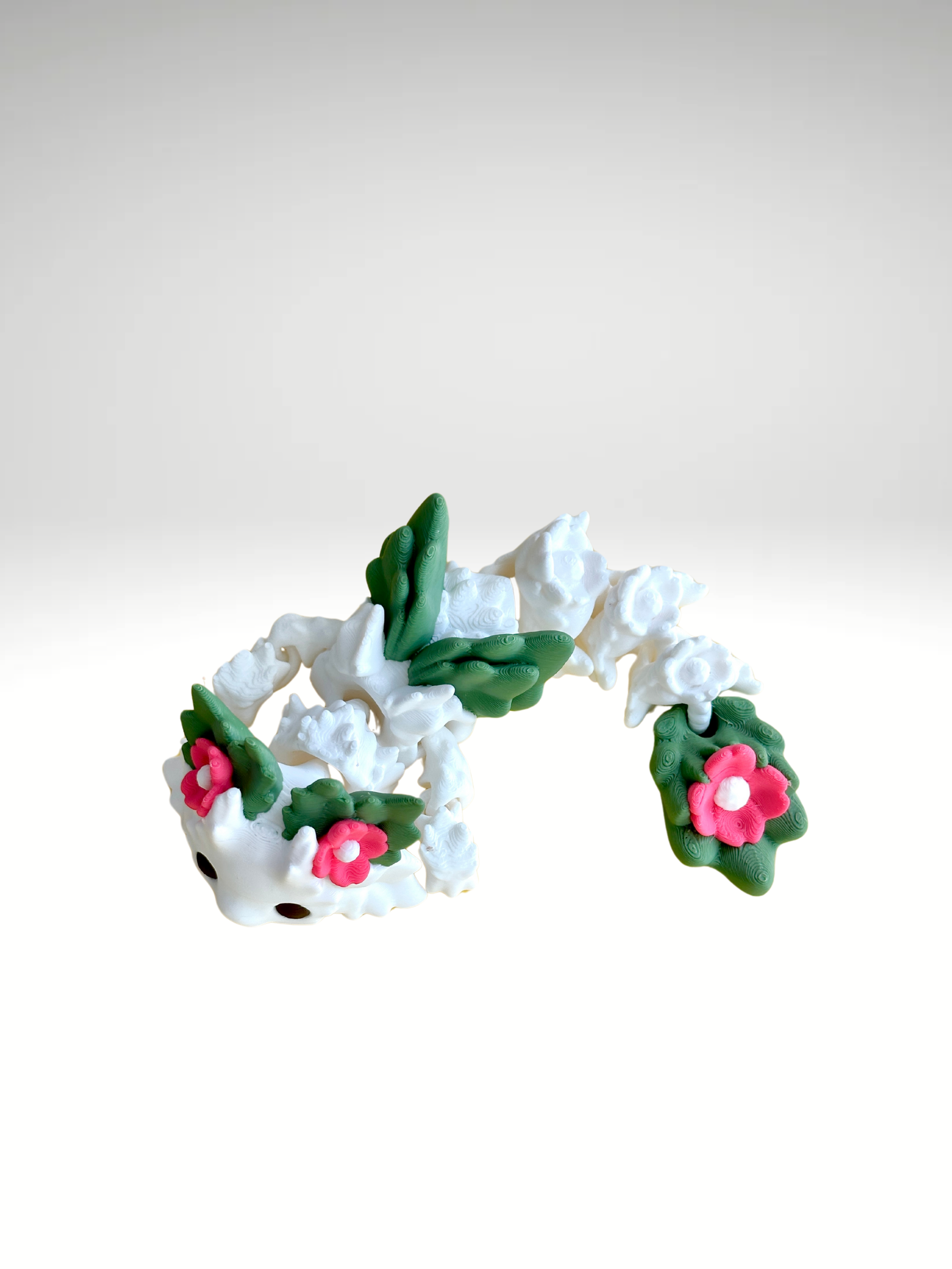 White 3D printed flower dragon charm with pink floral details and green leaf-like spots, laying flat