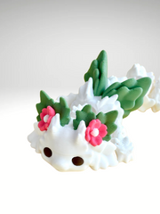 White 3D printed flower dragon charm with pink floral details and green leaf-like spots, laying flat
