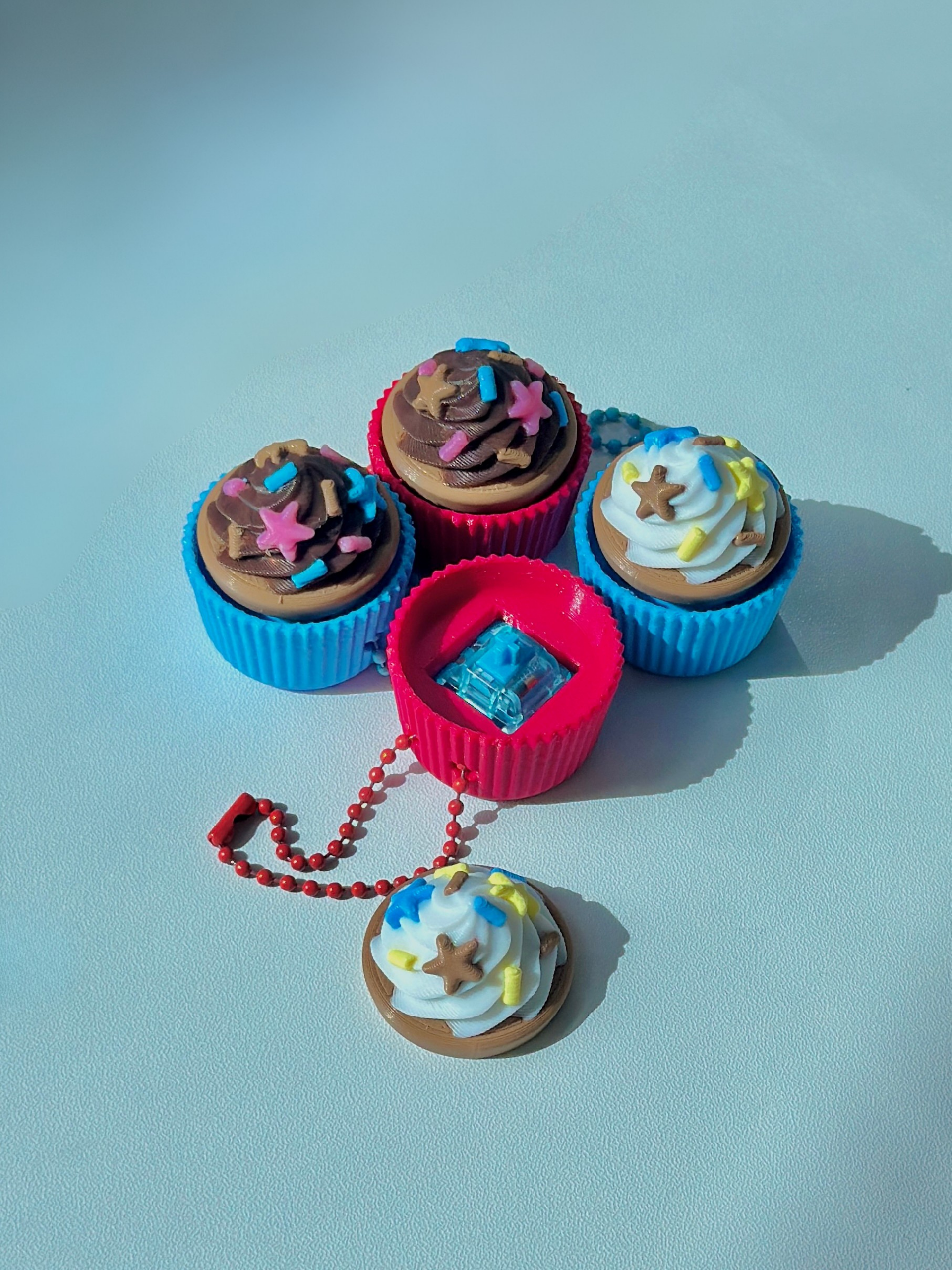 Set of four 3D printed cupcake fidget toy keychains including two chocolate and two vanilla, with one cupcake opened to show the internal key switch mechanism