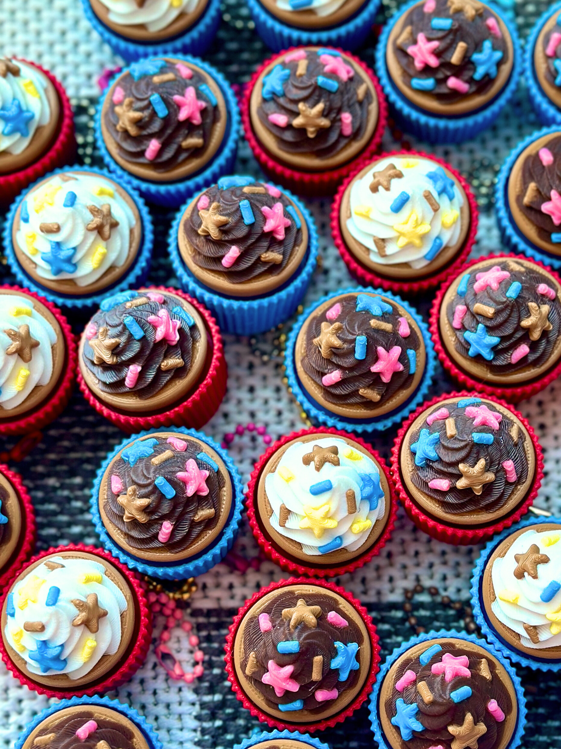 Several chocolate and vanilla cupcake clicker keychains scattered on a table surface, styled for a dessert-themed display
