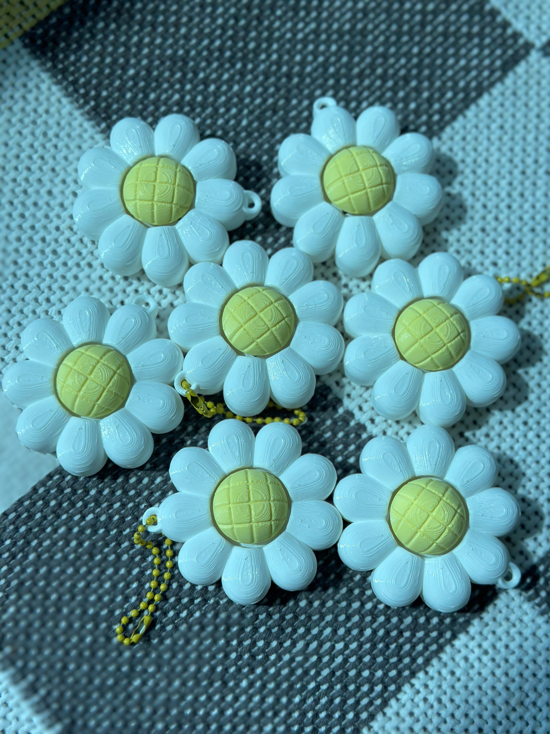 Several daisy flower clicker keychains arranged on a surface, showing their white petal design and yellow centers