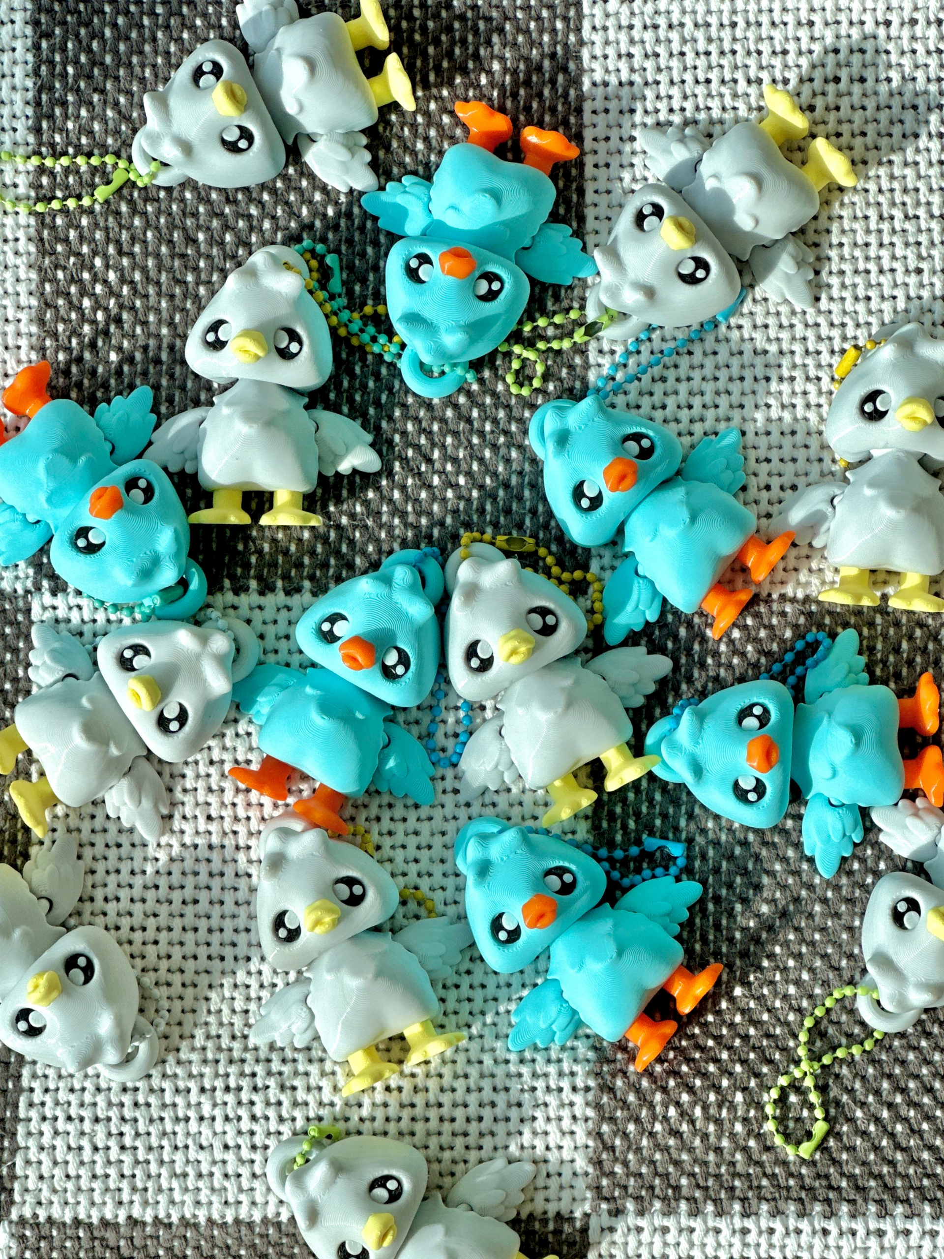 Multiple 3D printed goose bag charms scattered on the floor, showcasing blue and white variants with colorful beaks and feet