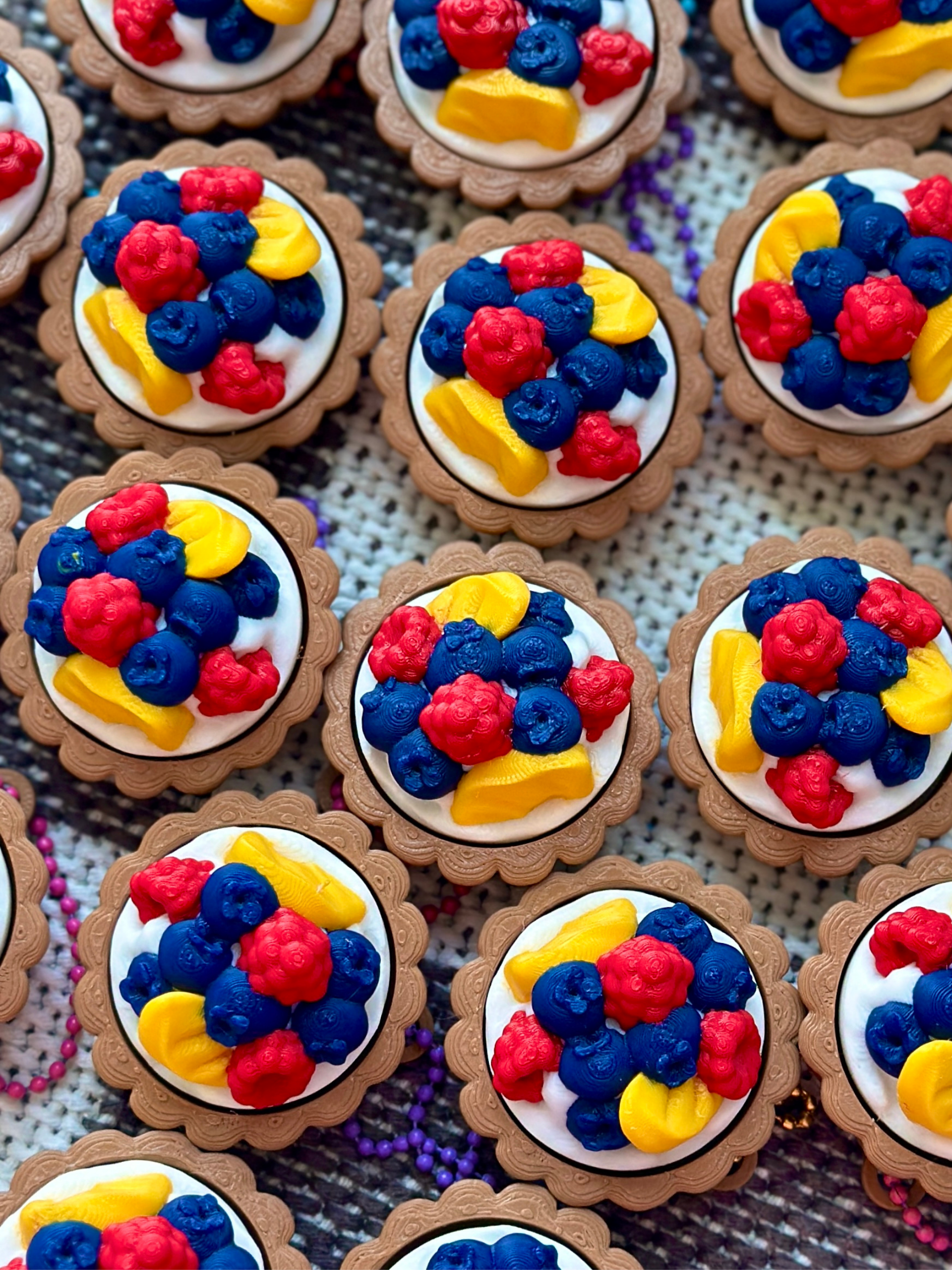 Multiple fruit tart clicker keychains arranged on a flat surface, showcasing colorful fruit designs and round tart shape