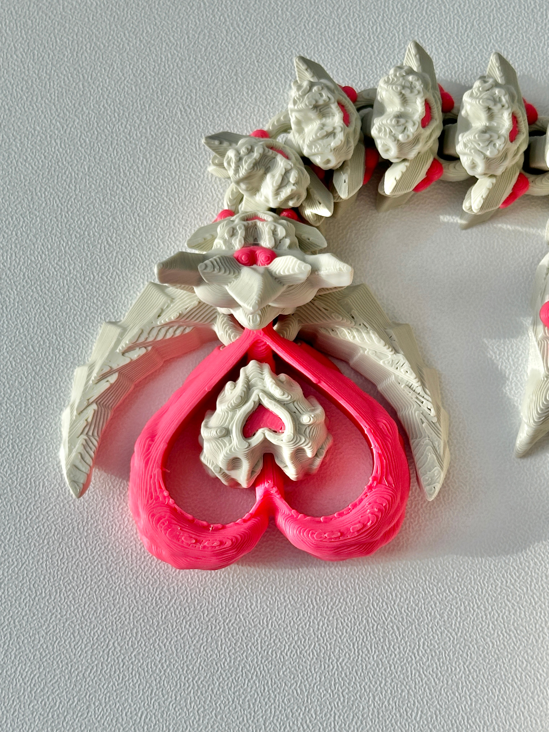 Close-up of the Heart Dragon’s tail showing a pink heart-shaped tip with a small beaded heart center, surrounded by feather-like textures