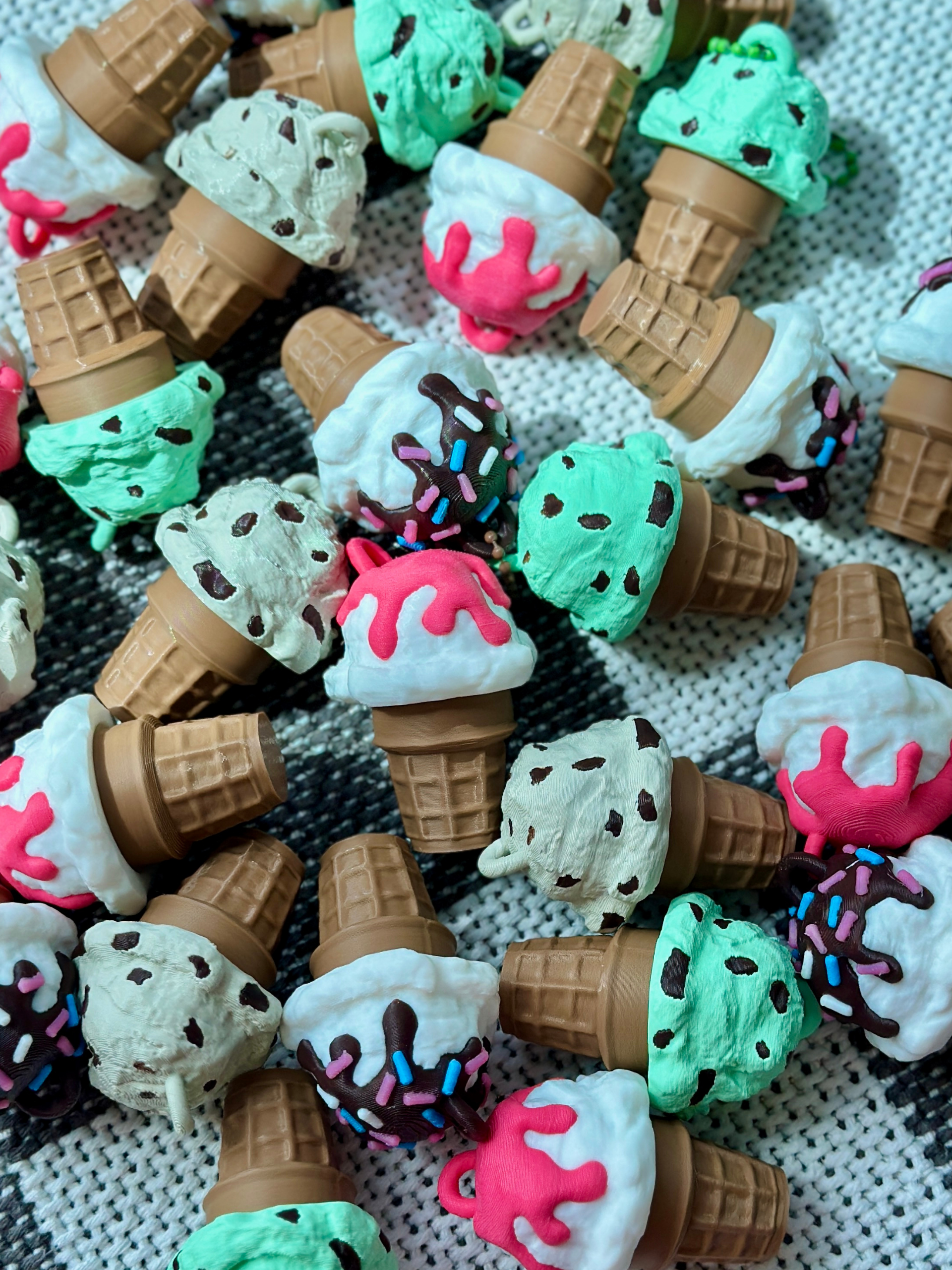 Several 3D printed ice cream cone clicker keychains arranged flat on a surface, showcasing various colorful swirled designs