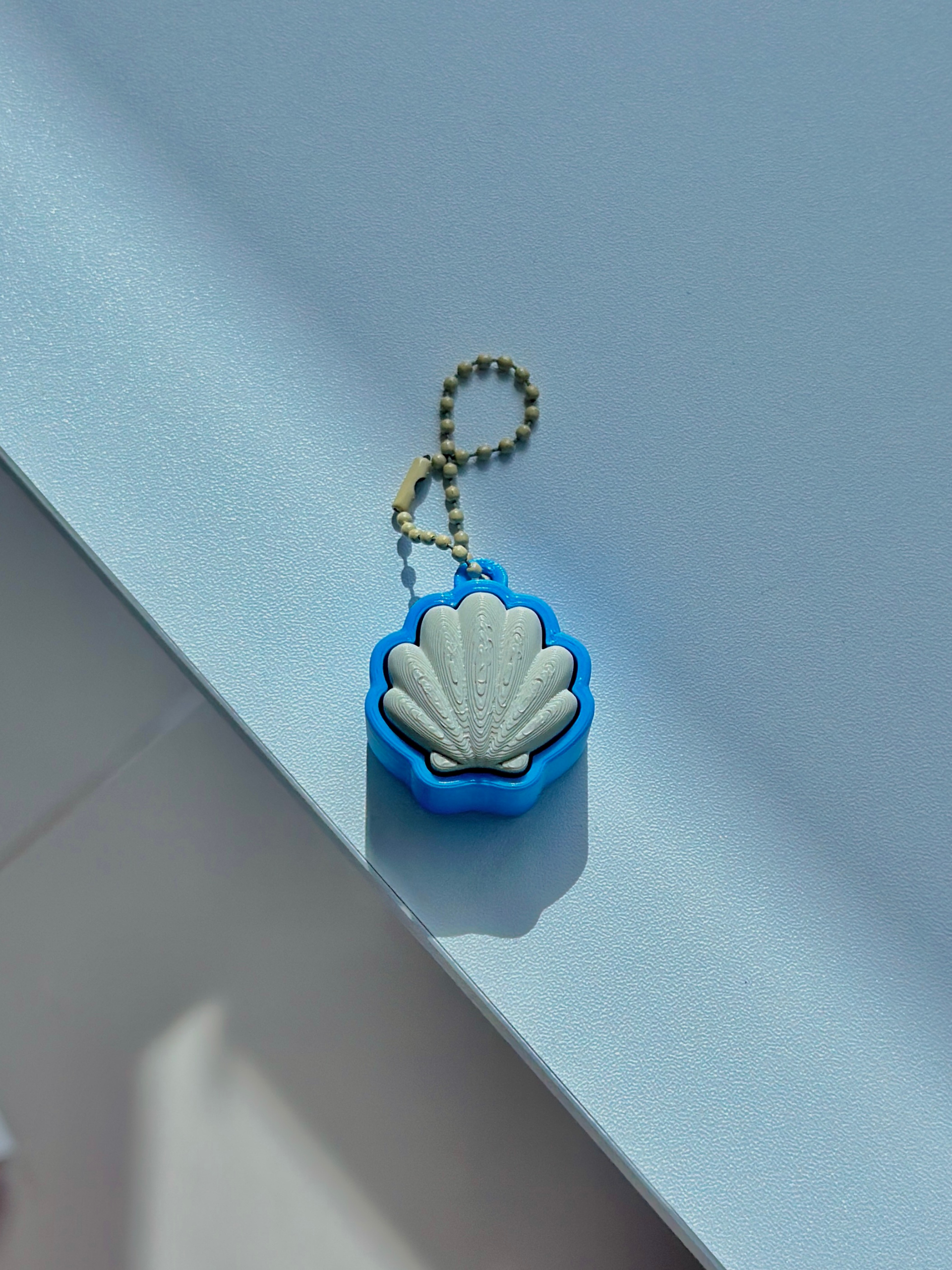 3D printed seashell-shaped fidget clicker keychain with soft ridges, displayed on a white background