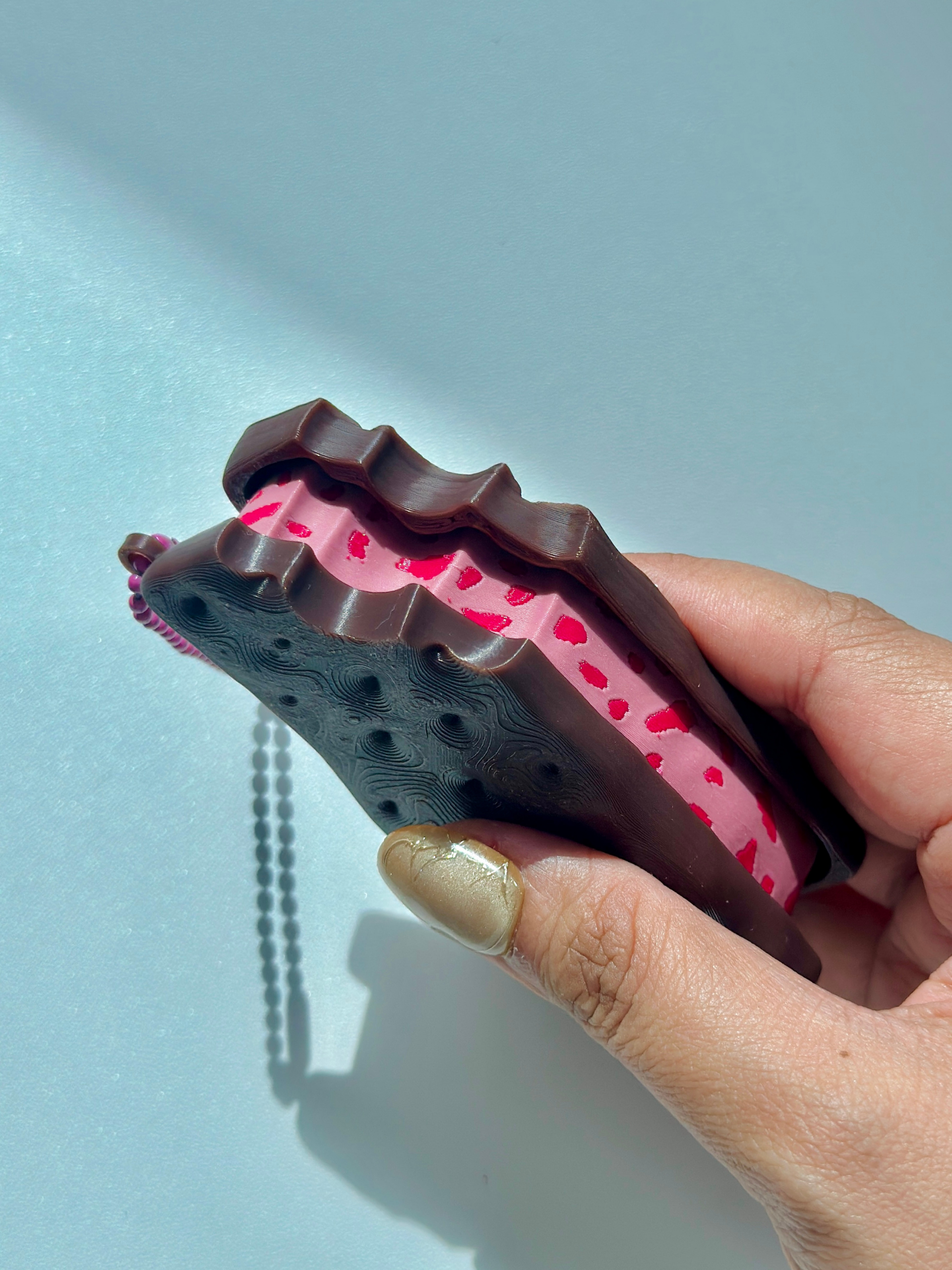 Strawberry ice cream sandwich fidget toy keychain held by hand, showing bite detail on the edge and textured biscuit surface
