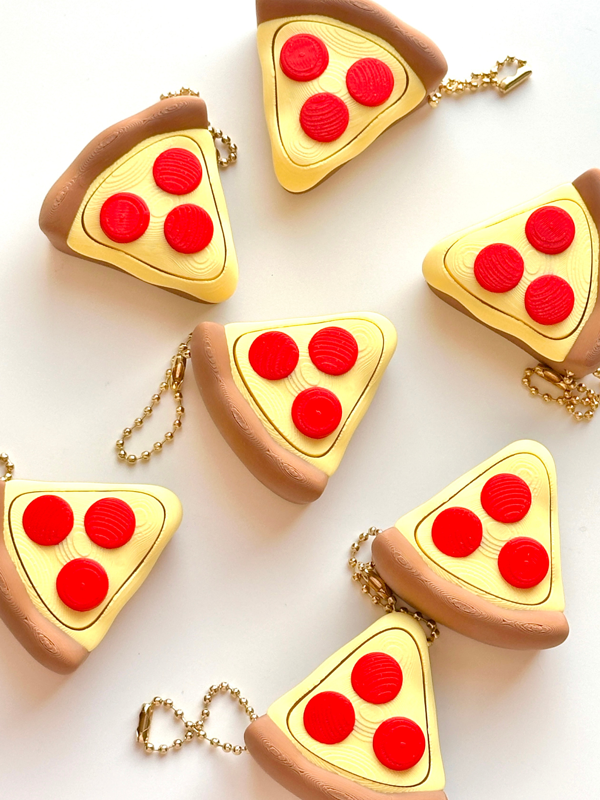 Pepperoni pizza slice clicker fidget keychains scattered on a white surface | Dubai 3D Printing
