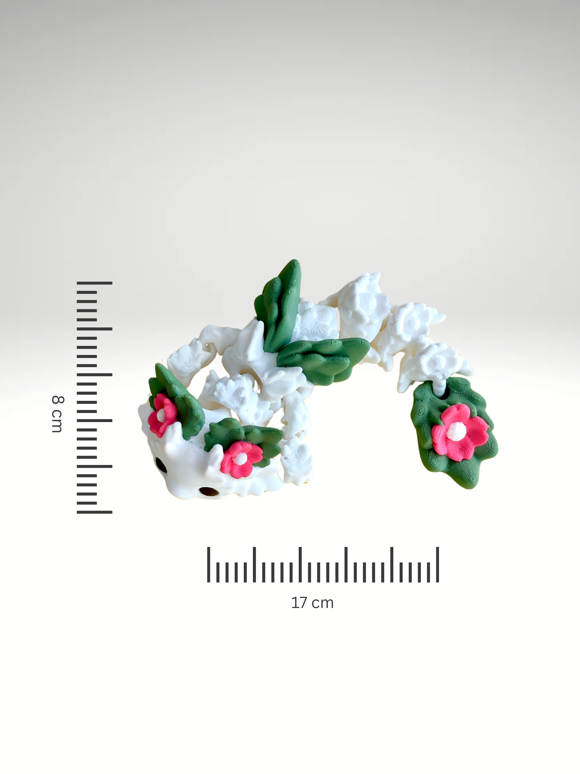White 3D printed flower dragon charm with pink floral details and green leaf-like spots, laying flat